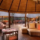 Exterior view of the Hoyo Hoyo Safari Lodge dining area, overlooking the bush. Comfortable seating is sheltered by traditional conical thatched structures.