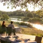 Guests enjoying views of the Sand river on an outdoor decked dining area, at Dulini River Lodge.