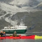 Kayakers enjoying exploring Glacier Bay in Alaska, with Wilderness Adventurer in the background.